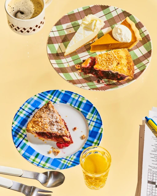 Overhead view of two plates with slices of pie and cake, accompanied by a cup of coffee, a glass of juice, and a crossword puzzle.