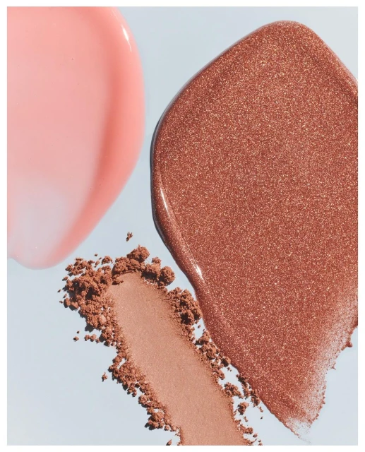 Cosmetic product swatches: glossy pink lip gloss, shimmery bronze highlighter, and neutral blush on a light blue background.