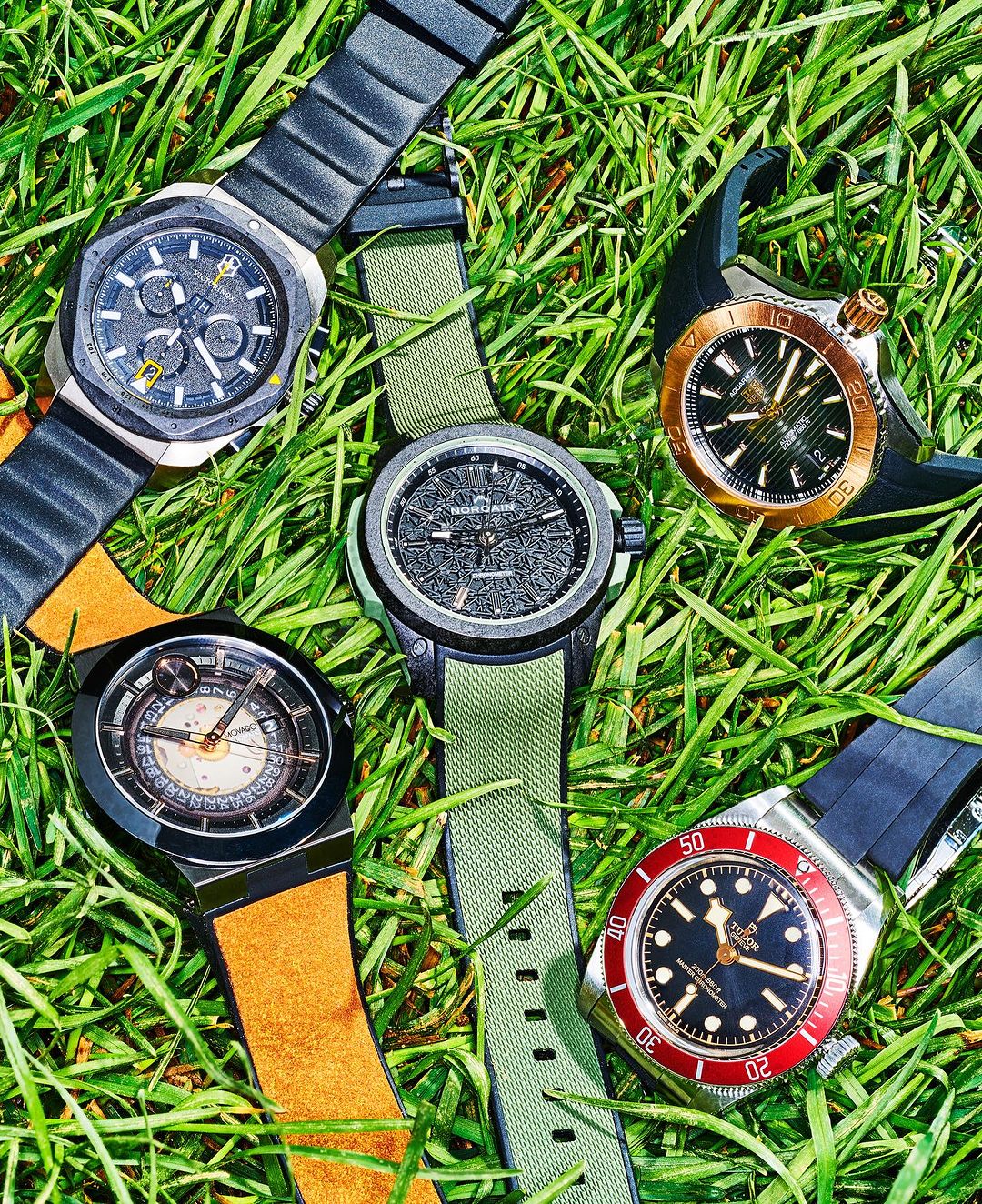 Five wristwatches with black and gold details on a bed of green grass, highlighting luxury timepieces and their aesthetic appeal.