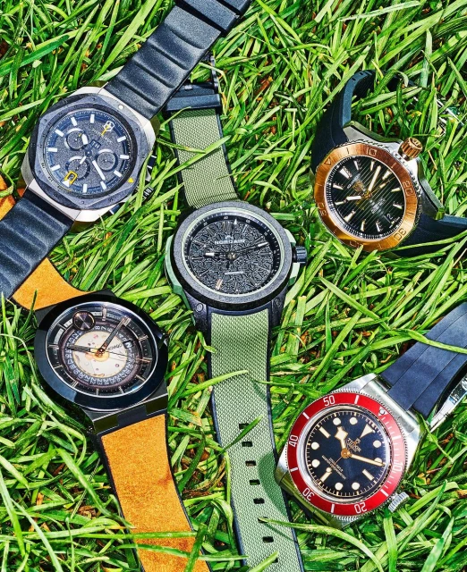 Five wristwatches with black and gold details on a bed of green grass, highlighting luxury timepieces and their aesthetic appeal.