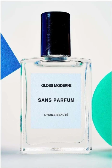 Clear glass perfume bottle with a black cap and a white label on a bright backdrop with blue and green geometric shapes.