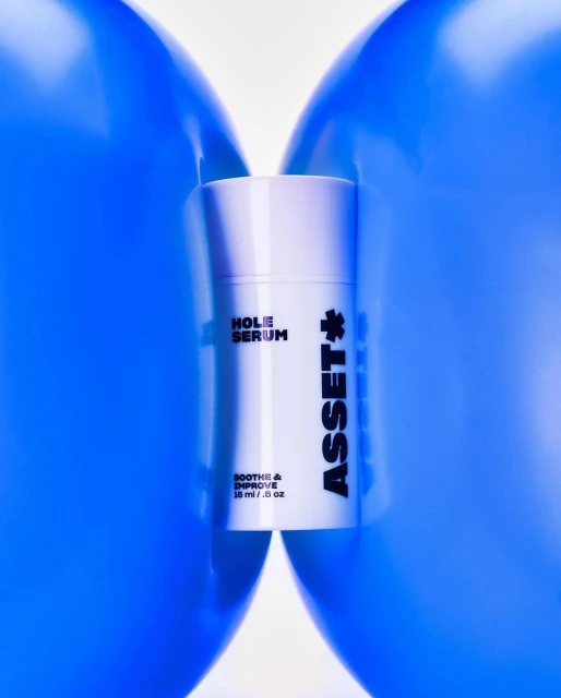 Product shot of a white tube of skincare between two blue balloons, featuring the text 'Hole Serum' and 'Asset'.