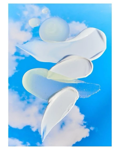 Cosmetic product smears against a blue sky with white clouds, displaying skincare textures and a beauty aesthetic with a clean backdrop.
