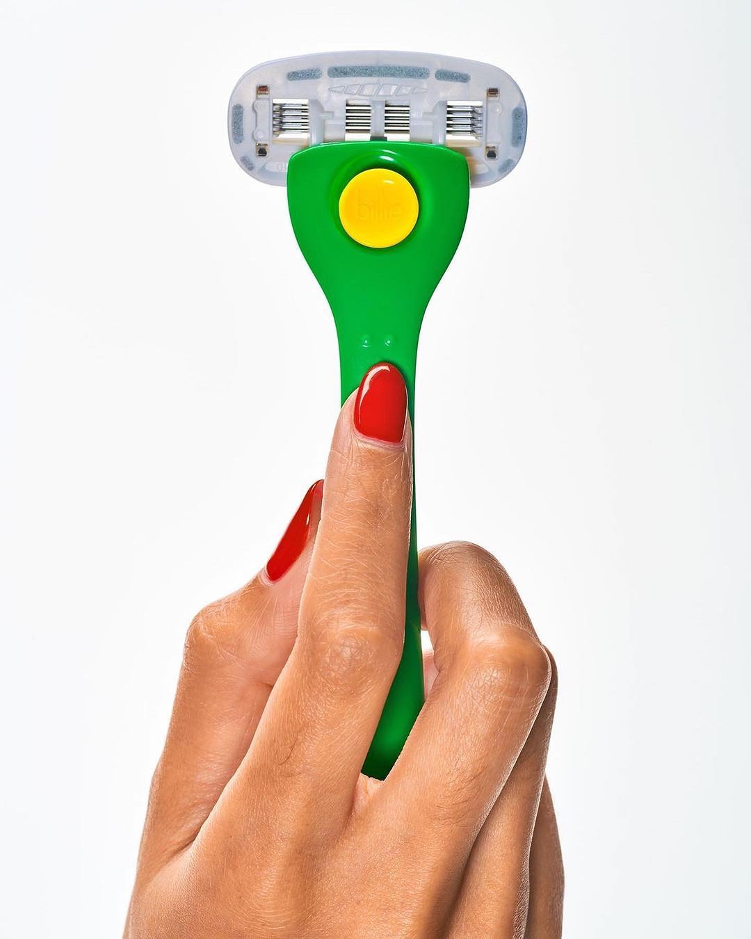 Close-up of a manicured hand holding a green and yellow razor against a white background, emphasizing product presentation.