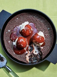 Overhead shot of chocolate dessert in a black cast-iron skillet with ice cream and chocolate sauce on a lime green surface.