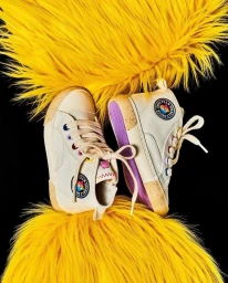 Two off-white high top canvas sneakers with purple soles framed by bright yellow faux fur against a black background.
