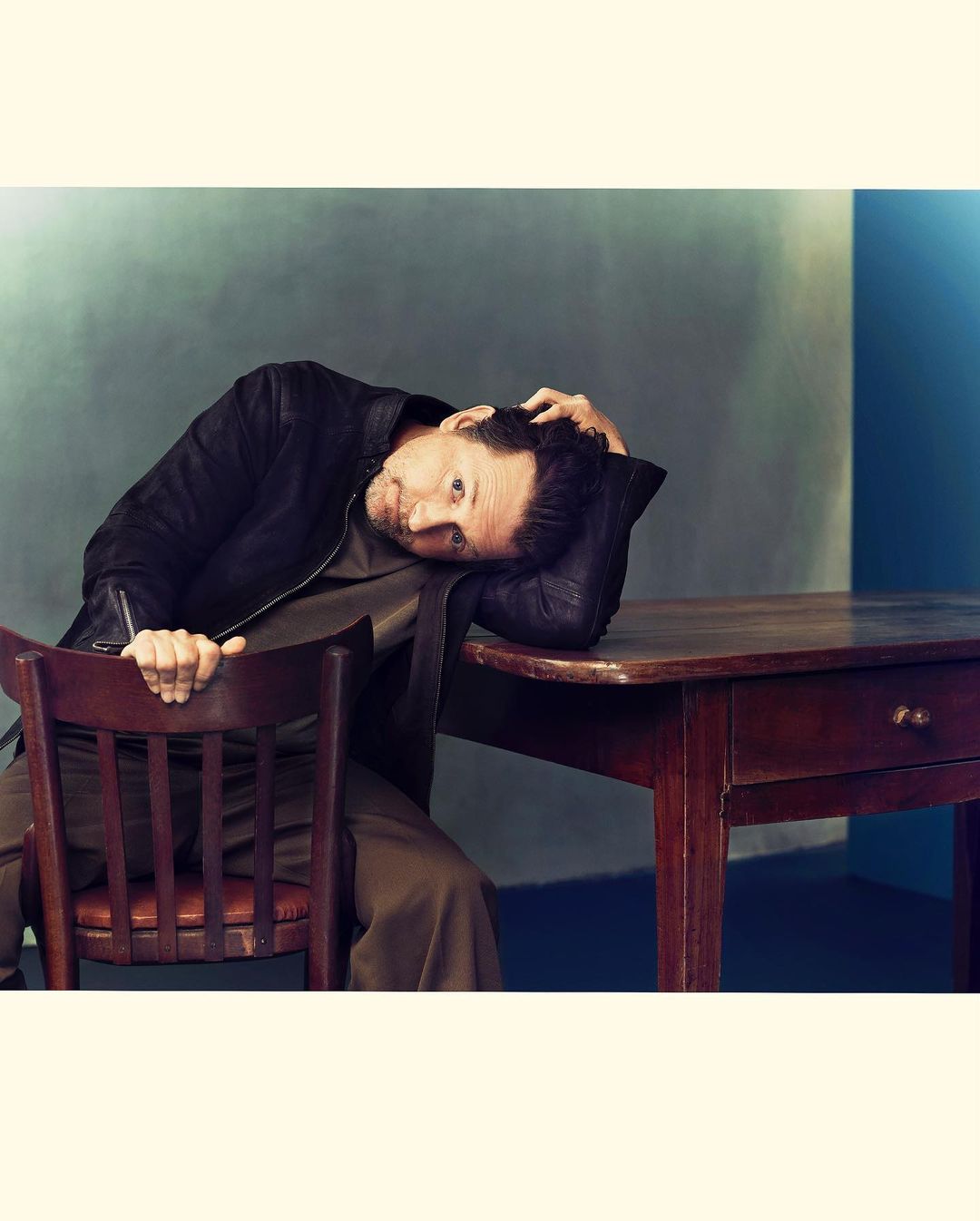 A man seated at a wooden table resting his head on his hand by photographer Joe Pugliese
