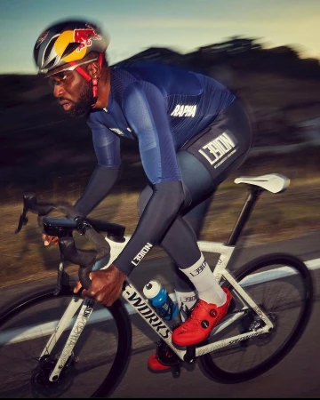 Focused African American cyclist in blue jersey and helmet races outdoors on a white bike, displaying fitness and determination.