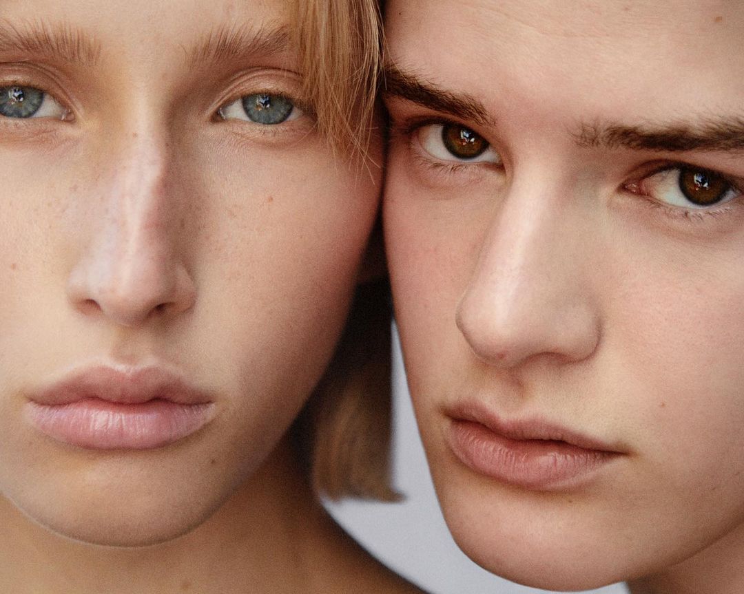 Close-up of two young faces, a fair-skinned woman with blonde hair and blue eyes, and a fair-skinned man with brown hair and eyes.