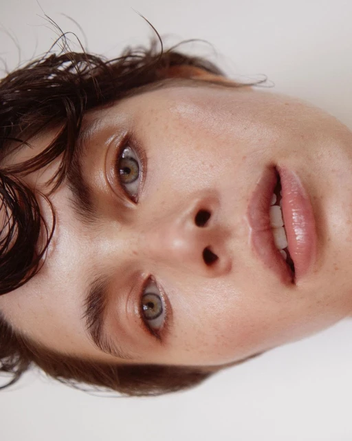 Close-up portrait of a young adult female with tan skin, light brown eyes, and dark brown hair, set against a clean, minimalist white background.