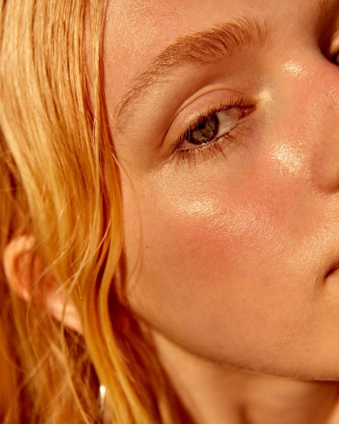 Close-up of a young woman with fair skin and golden hair, showcasing natural makeup and soft lighting in a beauty-focused portrait.