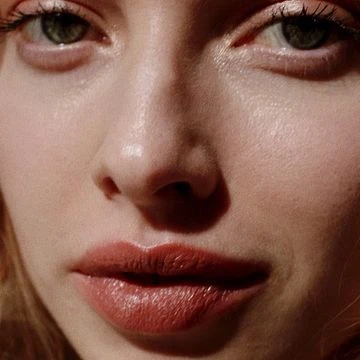 Close-up portrait of a woman with fair skin, light brown lipstick, and green eyes, capturing beauty and facial details.