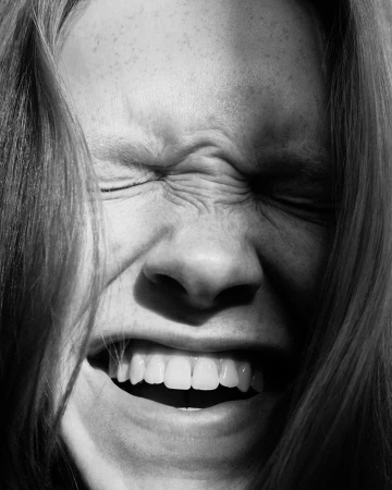 Close-up monochrome portrait of a person with tight squinted eyes and bared teeth by Johanna Nyholm