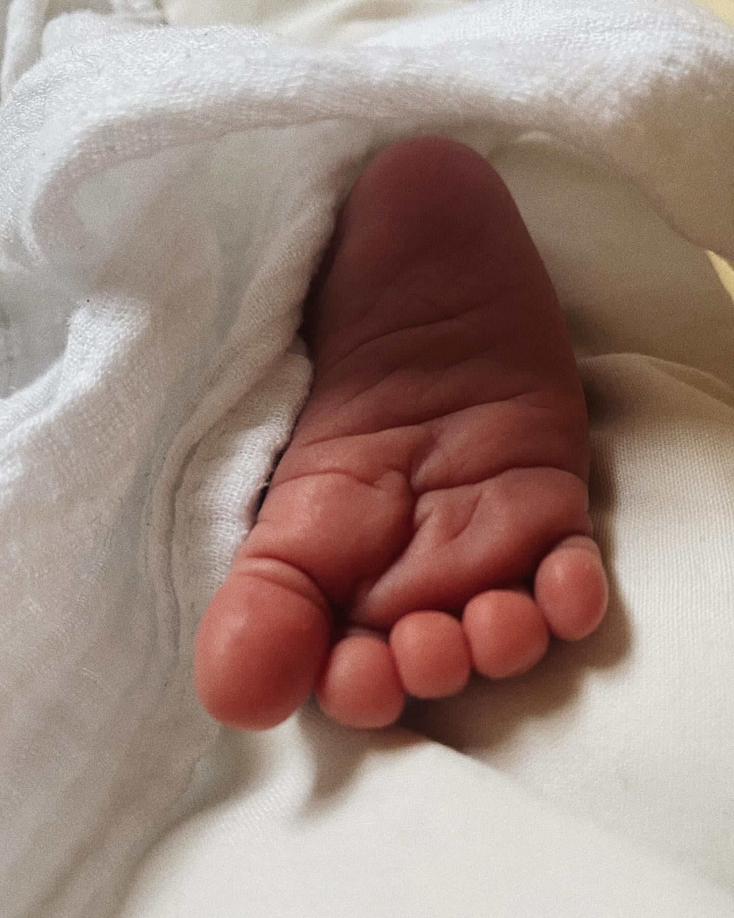 Close-up of a newborn baby's foot against a soft, white towel or blanket, highlighting the delicate skin and tiny toes.