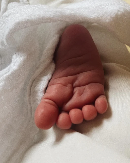 Close-up of a newborn baby's foot against a soft, white towel or blanket, highlighting the delicate skin and tiny toes.