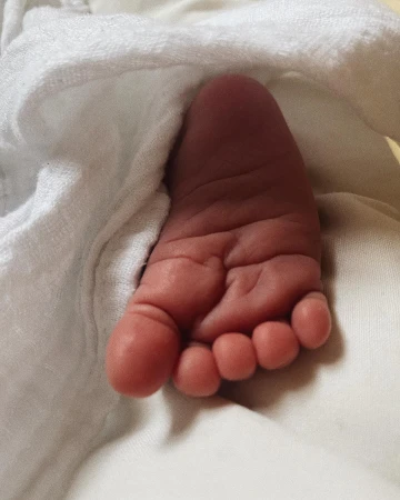 Close-up of a newborn baby's foot against a soft, white towel or blanket, highlighting the delicate skin and tiny toes.