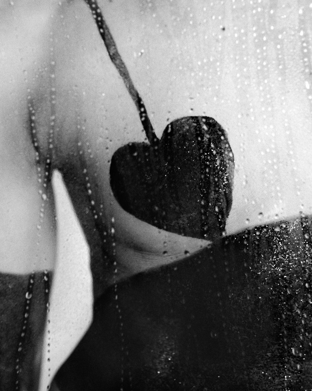 Artistic black and white photo of a woman's back and shoulder with water droplets on a glass surface in the foreground.
