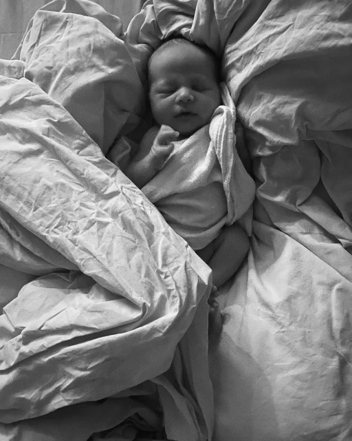 Monochromatic image of a newborn baby sleeping peacefully in a bed covered with soft, wrinkled linen, creating a serene and cozy scene.