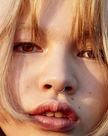 Close-up portrait of a young woman with blonde hair, freckles, and a silver septum ring in London by Johanna Nyholm.