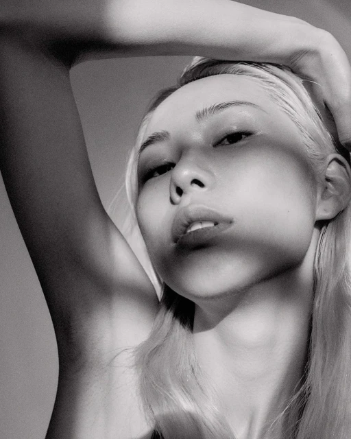 Monochrome portrait of a blonde woman with hand on head, eye-level angle, soft lighting, and neutral background in a beauty shot.
