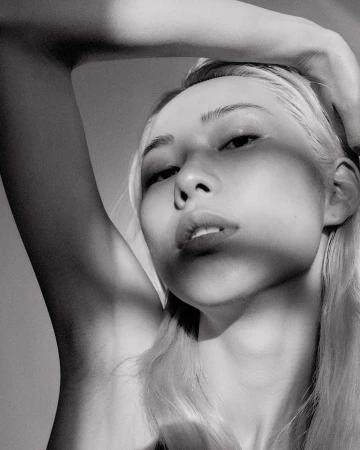 Monochrome portrait of a blonde woman with hand on head, eye-level angle, soft lighting, and neutral background in a beauty shot.