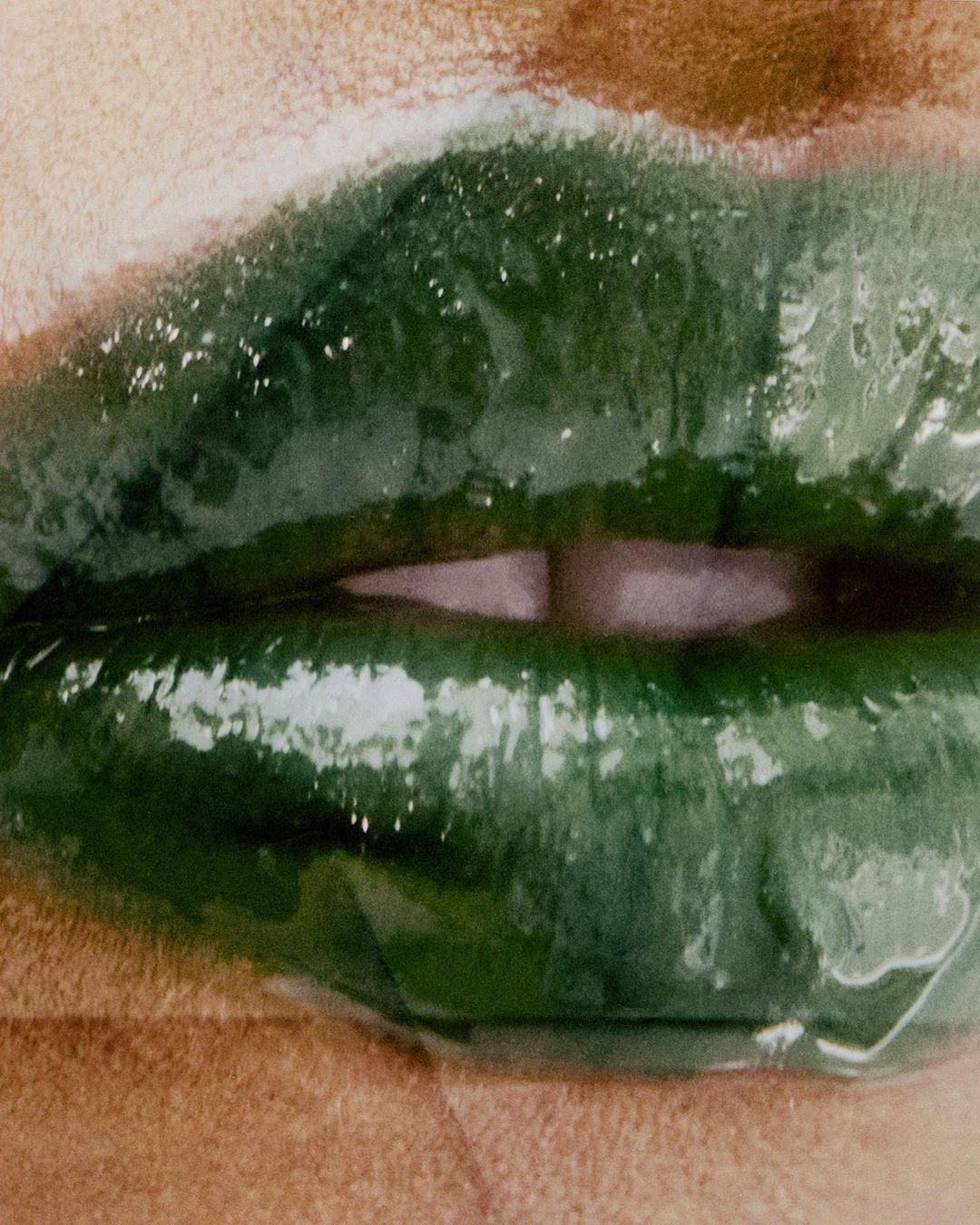 Close-up of a human face featuring lips covered in glossy, dark green lipstick, highlighting beauty and cosmetic details.