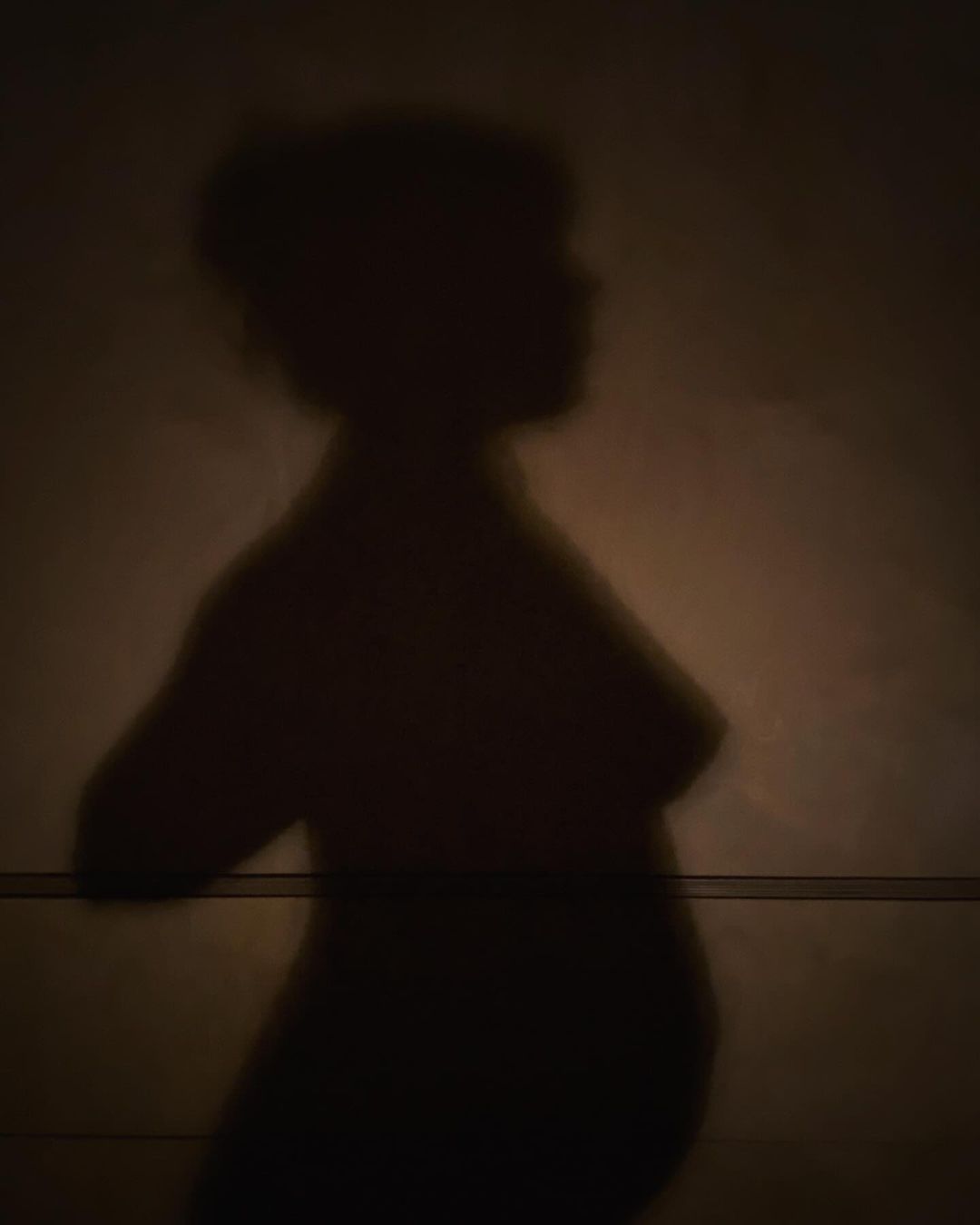 Striking silhouette of an adult female figure against a textured dark background with subtle light gradients, showcasing form and shadow.