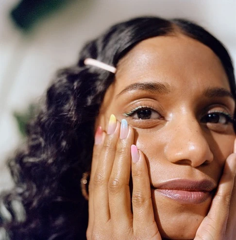Close-up portrait of a woman with dark, curly hair and pastel manicure, softly lit indoors, showing beauty and personal style.