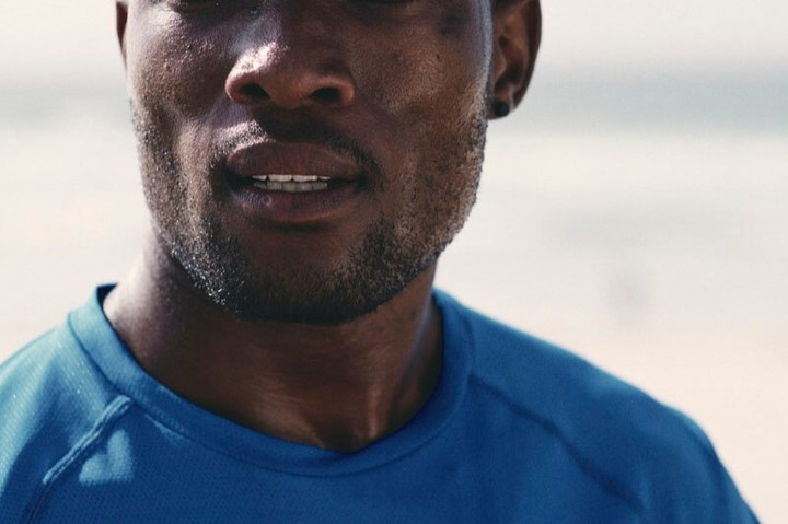 Close-up of a sweaty adult male wearing a blue shirt. He has dark skin, a short beard, and is likely involved in fitness or sports.