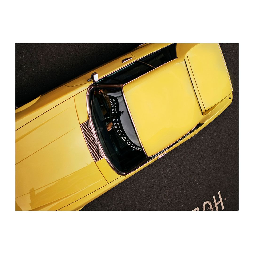 Overhead shot of a yellow vintage car, highlighting its sleek design and glossy finish against a dark surface.