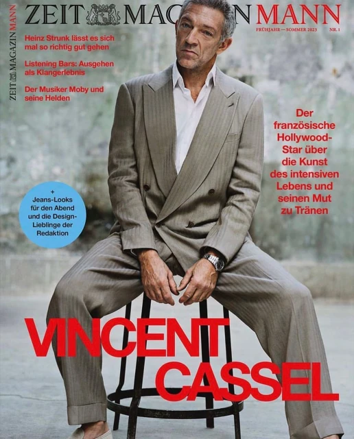 Magazine cover featuring a man in a suit sitting on a stool. The cover includes magazine titles and article headlines in German.