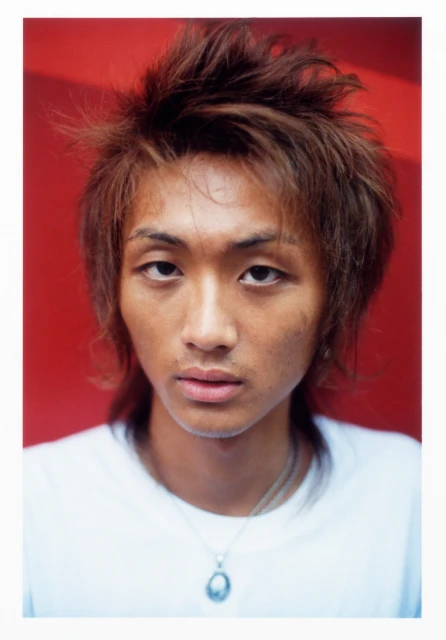Close-up portrait of an Asian adult male with brown hair and a white shirt against a red background, showcasing natural lighting.