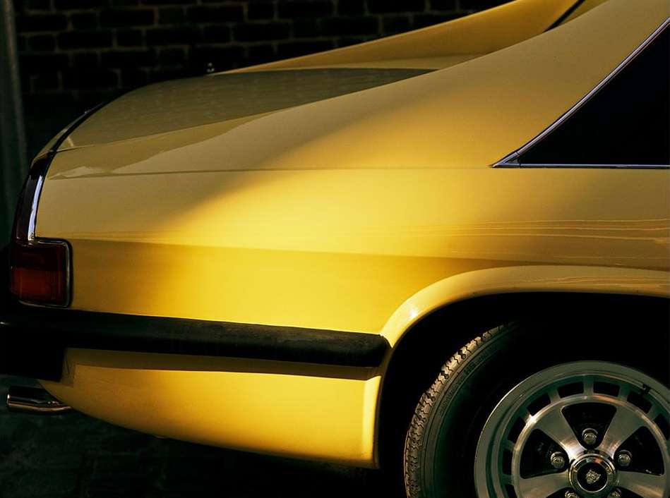 Close-up of a yellow Jaguar XJS coupe with chrome accents and black bumper, showcasing its sleek design and classic automotive styling.