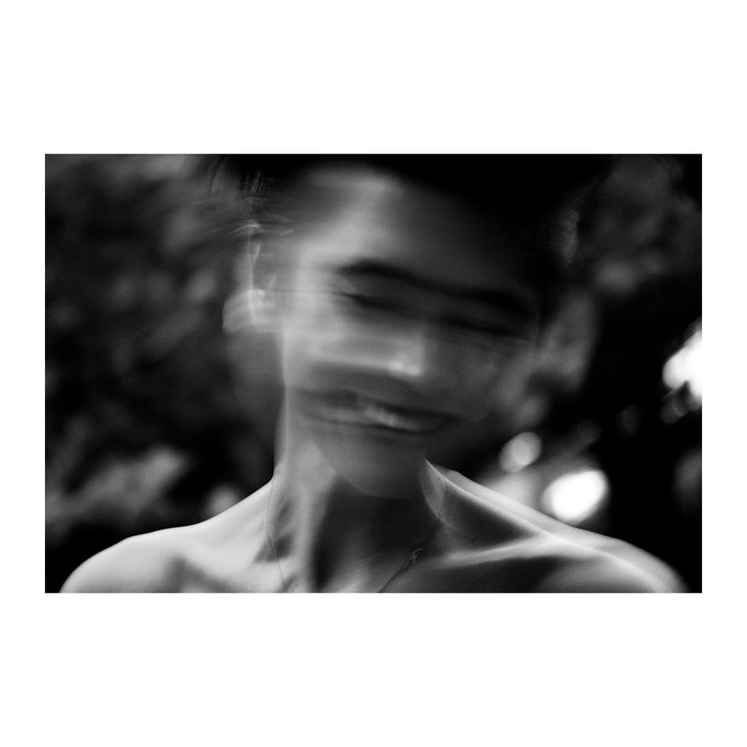 Black and white portrait of a blurred young adult with a shallow depth of field, appearing androgynous with short hair in an outdoor setting.