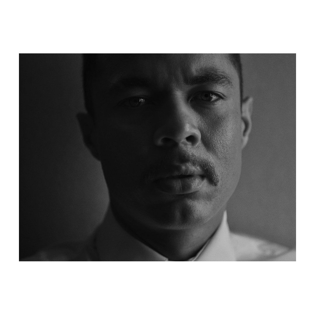 Striking black-and-white portrait of a man with a mustache, captured in a close-up shot with dramatic, contrasting lighting.