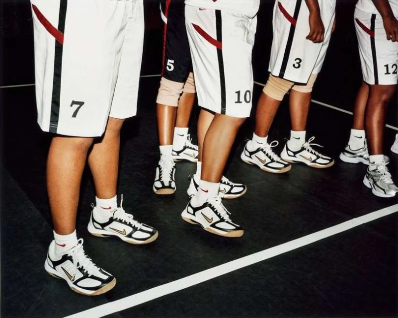 Close-up of basketball team legs and feet. Players wear white shorts with numbers and athletic shoes on an indoor court with a white line.