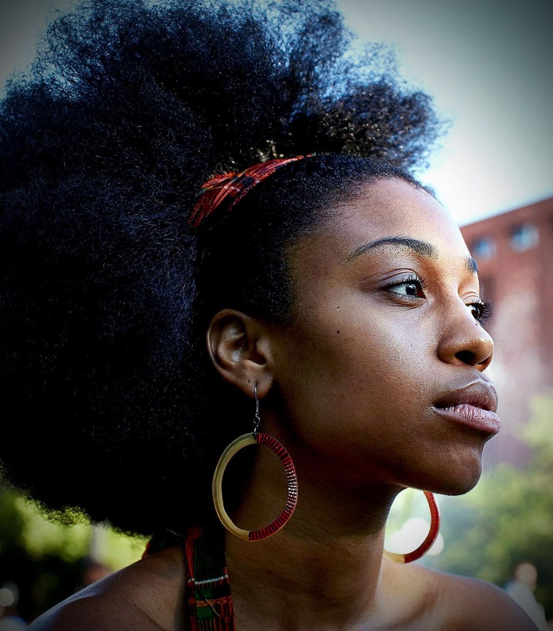 Profile portrait of a black woman with large voluminous hair and hoop earrings outdoors
