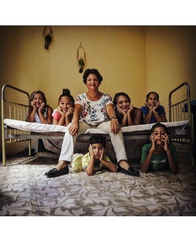 Family portrait featuring a group of six children with an adult female on a bed, in an indoor setting with warm lighting.