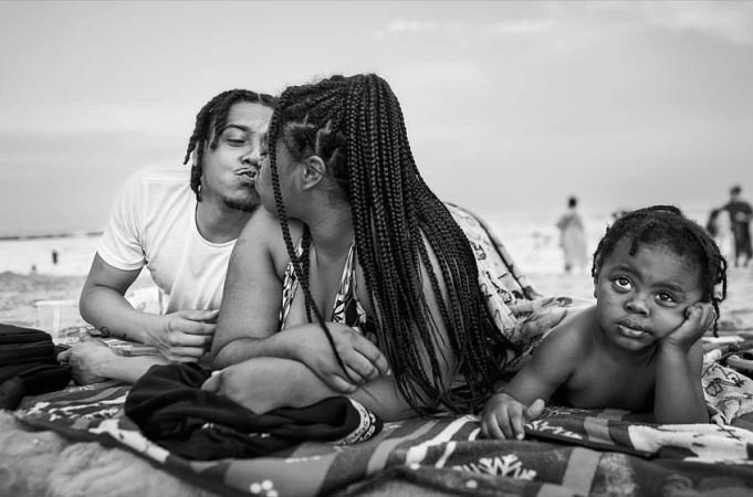 Black and white portrait of a family relaxing on a beach blanket, with a young child looking towards the camera.