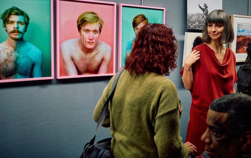Art gallery visitors admire framed photographic portraits on display, creating a cultural and social experience in an indoor setting.