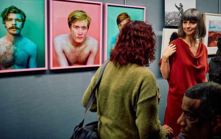 Art gallery visitors admire framed photographic portraits on display, creating a cultural and social experience in an indoor setting.