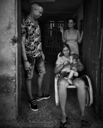 Black and white portrait of a family gathered in a doorway by John Blais, featuring a seated woman holding a young child.