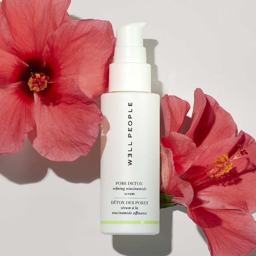 Cosmetic serum bottle by Well People with hibiscus flowers on a white background. Product shot for skincare and beauty brands.