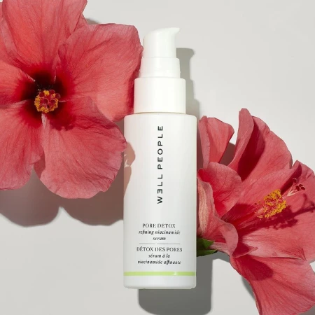Cosmetic serum bottle by Well People with hibiscus flowers on a white background. Product shot for skincare and beauty brands.