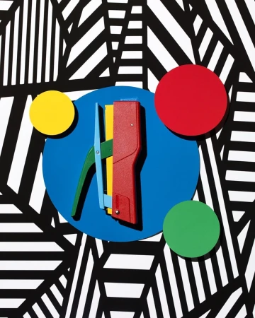 Close-up studio shot of a colorful tool with red, green, blue, and yellow elements against a graphic black and white pattern background.