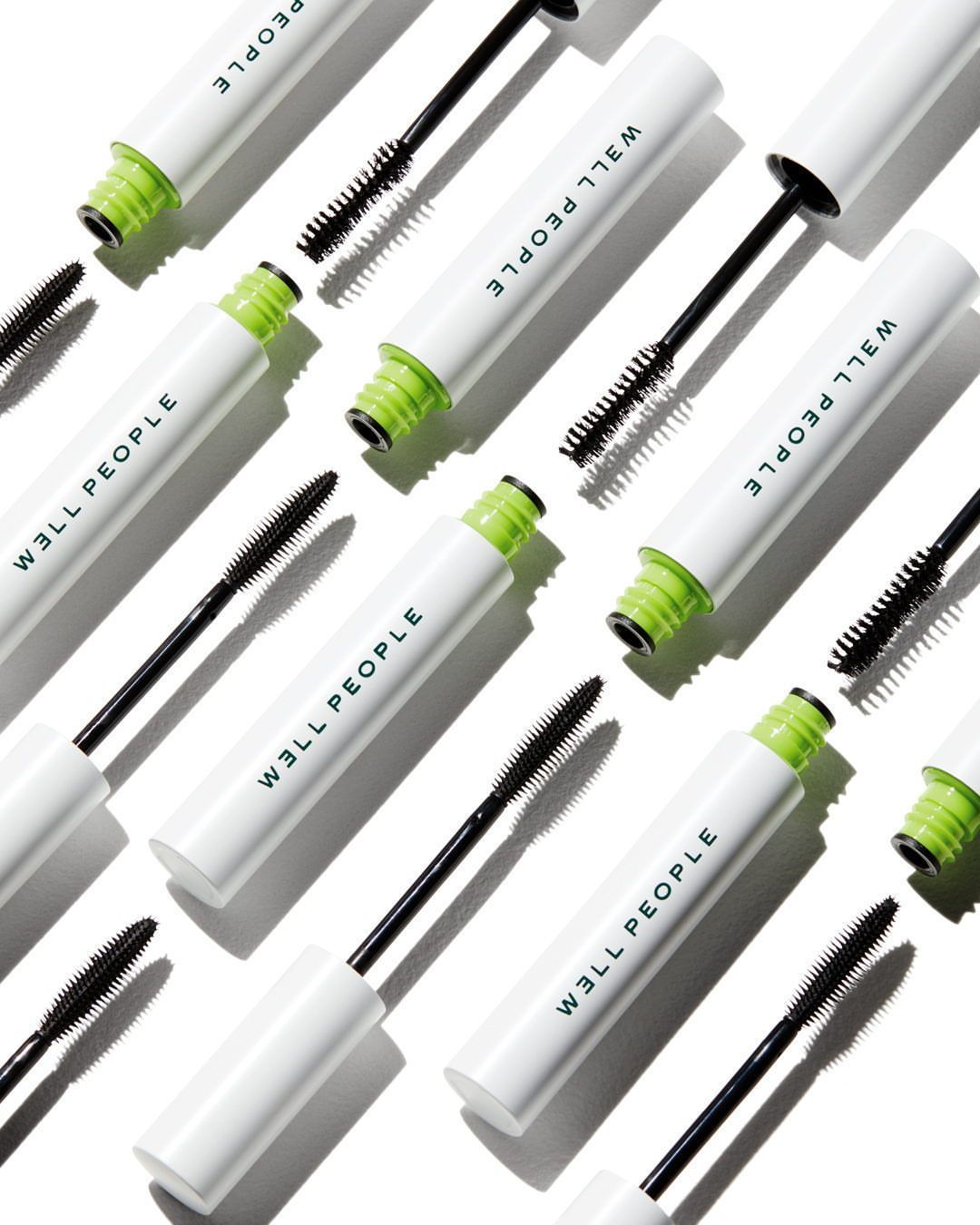 Overhead shot of multiple tubes of WELL PEOPLE mascara with black wands against a white background in a beauty product flat lay.