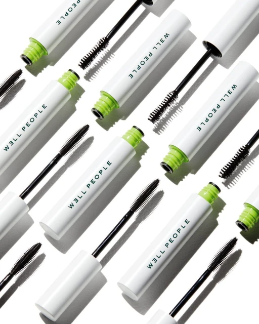 Overhead shot of multiple tubes of WELL PEOPLE mascara with black wands against a white background in a beauty product flat lay.