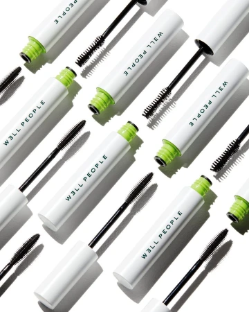 Overhead shot of multiple tubes of WELL PEOPLE mascara with black wands against a white background in a beauty product flat lay.