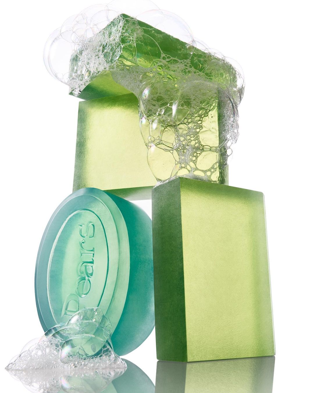 Close-up of stacked green transparent soap bars and oval soap with bubbles against a white background, product photography.