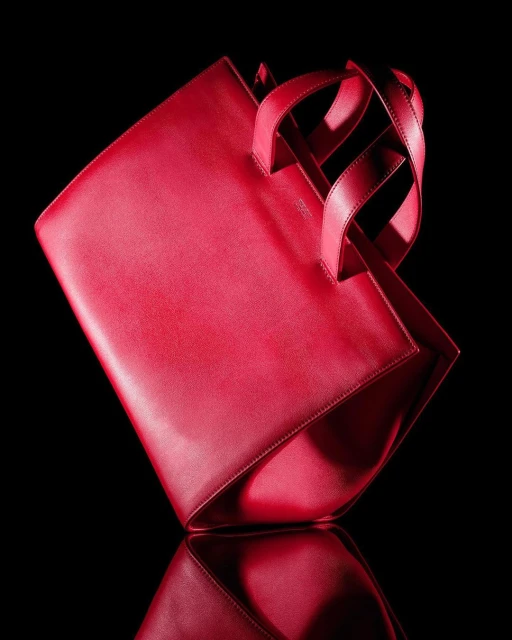 Red leather tote bag on a reflective black surface, showcasing its shape and design against a dark background.